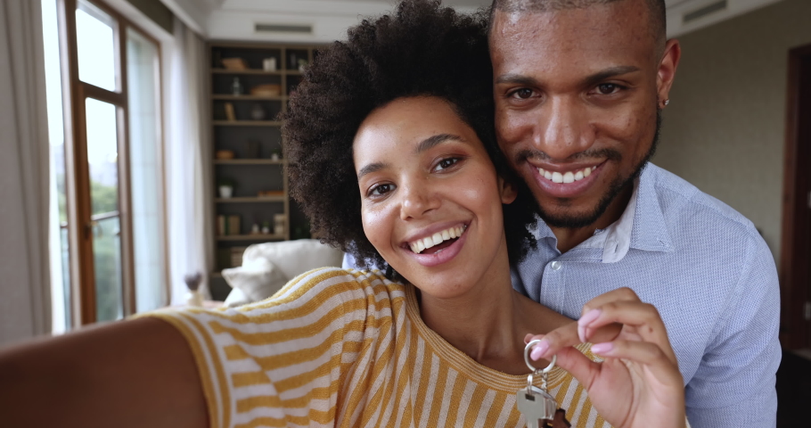 Excited African American couple modern apartment renters tenants hug hold keys shoot video on phone. Webcam portrait of overjoyed young husband wife share great news of getting mortgage or buying flat | Shutterstock HD Video #1085648348