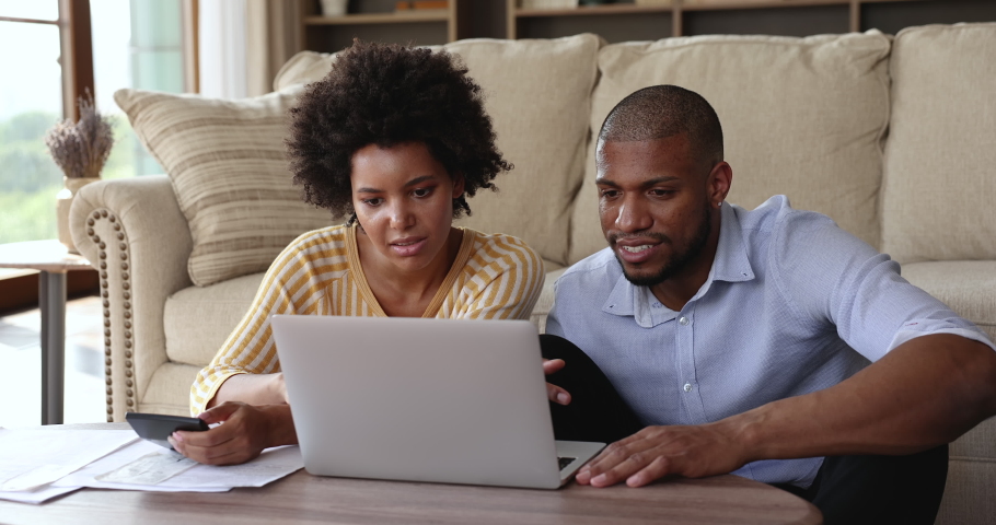 Focused Afro American spouses sit by laptop at home office calculate bills to pay online manage family finances engaged in budgeting work. Young couple prepare loan mortgage payments plan investment Royalty-Free Stock Footage #1085648381