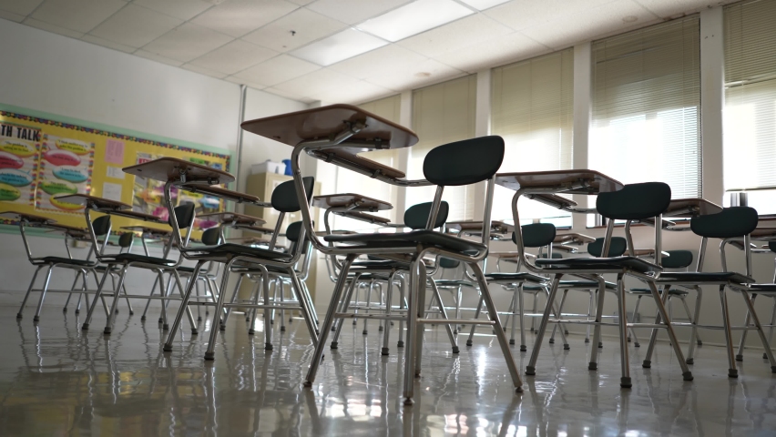Desks in empty dark high, middle, or elementary school classroom with light coming through windows. Royalty-Free Stock Footage #1085653184