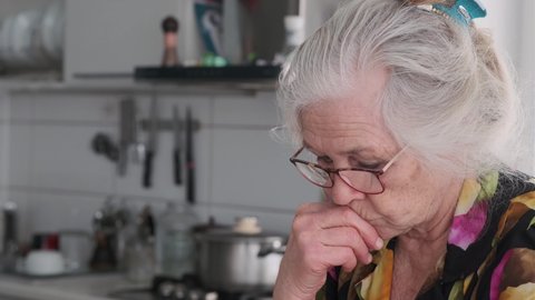 Elderly woman with gray hair wearing glasses in home kitchen, close up. Grandma talking via video link.