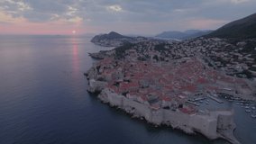 Drone video of a beautiful sunset in Dubrovnik with a fiery red sun, with ships sailing, frontal shoting forward.
