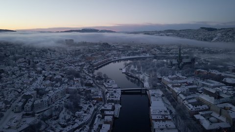 Sunrise Over The City Of Trondheim In Trondelag County In Norway With View Of Nidaros Cathedral, Old Town Bridge, And River Nidelva In Winter. wide aerial