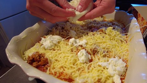 Mozzarella Cheese Being Sprinkled Into Lasagne Dish By Hand. Close Up, Low Angle