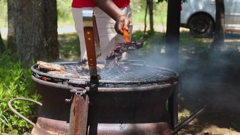 Close up view of the frying chicken in an open fire, with people cooking meat on top known as a braai stand. Braai or barbeque in nature background at Harare, Zimbabwe.
