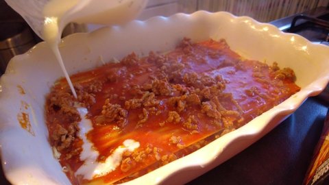 Bechamel Sauce Being Poured On Top Of Hot Bolognese Inside Lasagne Dish With Cheese Being Sprinkled After. Close Up