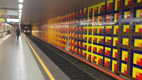 Brussels, Belgium - January 15, 2022: Brussels STIB-MIVB metro train arrives at Merode subway station. People on platform. It is a station for number 1 (purple) and 5 (yellow) lines. Tiles decoration