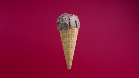 Rotating chocolate ice cream ball in waffle cone on red background. Soft cream cone close-up. Gelato icecream scoop in waffle cone over colorful background