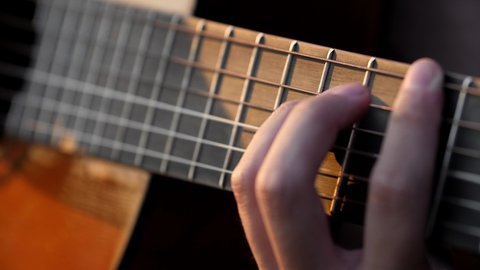 Closeup of musician's fingers strumming on acoustic guitar strings in the sunset
