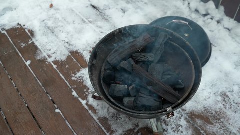 Burning fire in a round small barbecue. In the courtyard of the house, in winter. top view.Man is circumcised. Blows up the fire.