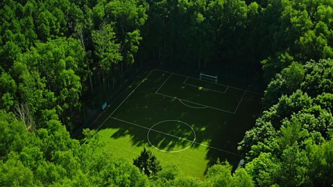 Aerial drone reveal shot of hidden secret football field in middle of green lush forest or park. Incredible and beautiful travel destination. Sport field 