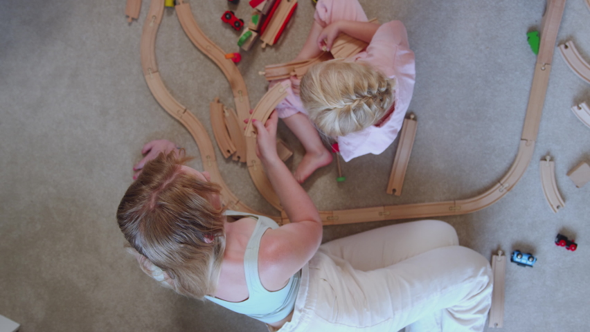 Overhead Shot Of Mother And Daughter At Home Playing With Wooden Train Set Toy On Carpet