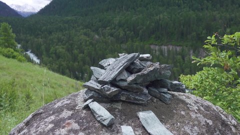 Oil shales from the Altai Mountains. A pile of slate on the background of a mountain forest valley (gorge) with stormy river, grassland and distant snow-capped peaks
