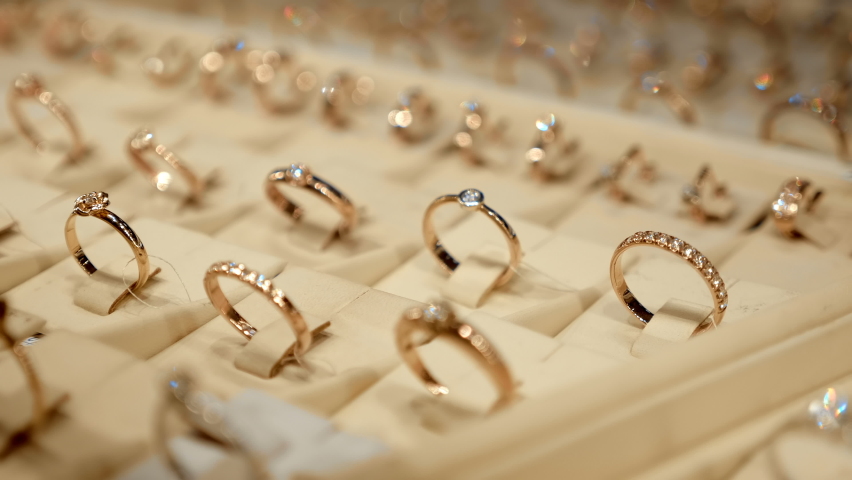 Rows of beautiful expensive fashionable gold rings behind the glass of a jewelry store window shine brightly with their diamonds. Shot in motion. Closeup Royalty-Free Stock Footage #1085687579