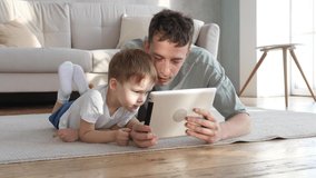 Happy father and cute preschool son using tablet watching cartoon enjoying watching funny social media video shopping online relaxing at home together
