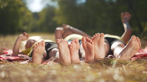 happy family. close-up of a kids leg feet lie on the grass in the summer park. children feet close-up team together happy childrens friendship. children lie in the park on sun the grass family