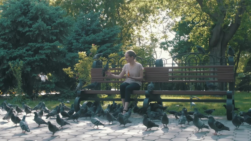Young happy girl feeding pigeons in the park on a bench.