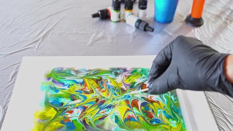Drawing process with alcohol ink on liquid. A female hand in a glove with a wooden stick makes a drawing on the surface. Bright colors. Beautiful patterns.