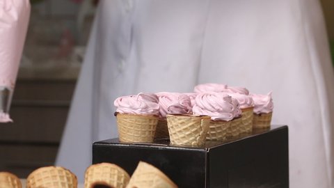 Wafer cones smeared inside with liquid chocolate. They are on stands. A woman fills cones with marshmallows from a pastry bag. We make horns with chocolate and marshmallows. Close-up.