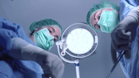 From below female surgeons in medical uniform using professional tools while standing under bright light in operating theater. High quality 4k footage