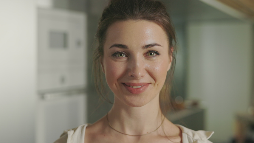 Happy caucasian woman covering eyes with cherry tomatoes while smiling and looking at camera on domestic kitchen. Portrait of joyful young woman.
