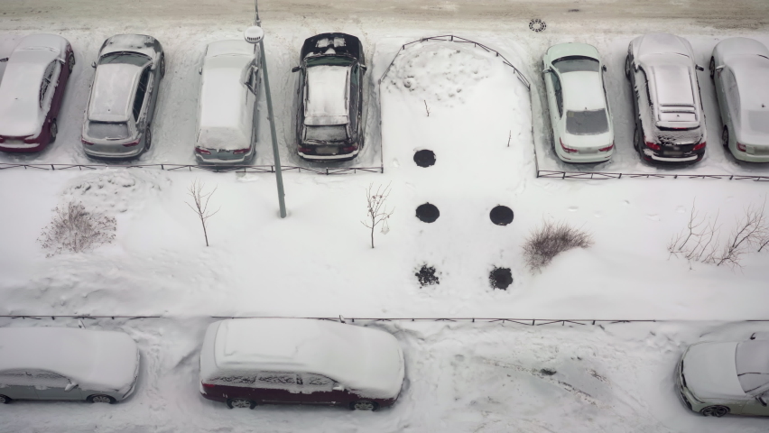 Snowy winter in the city. Top view of the parking lot in the courtyard of a residential building. The road is covered with white snow, the car is moving. Frozen town.
