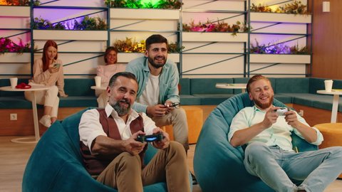 Two younger men and an older looking man are playing video games while sitting in bean bag chairs and cheering each-other on. Arri Alexa Mini.