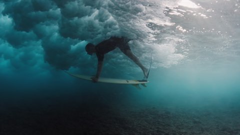 Surfing in Maldives. Man dives with surf board underwater to pass the ocean wave