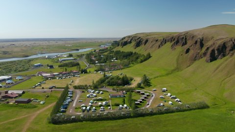 Camping site and village in countryside near elevated ridge with rocky escarpment. Sunny day with clear sky. Iceland
