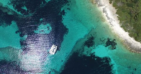 Aerial, top scene of transparent doted shore of a virgin island. Catamaran anchored. Rocky coastline. Paradisiac landscape. Caribbean shore. Drone scene, from aerial to a detail of catamaran.