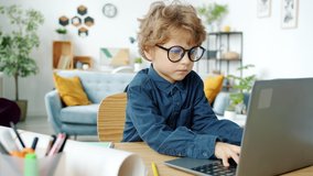Serious kid in eyeglasses working with laptop computer sitting at desk at home concentrated on online activity. Technology and childhood concept. - Powered by Shutterstock - Get 15% off with code: PIKWIZARD15