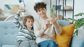 Young woman and little boy making online video call with smartphone talking and laughing waving hand sitting on couch at home. People and communication concept.