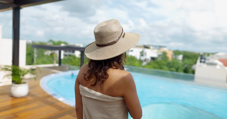 Beautiful woman in bikini and hat walking towards pool while taking off her towel in slow motion.Attractive woman from behind on poolside with cloudy horizon as background. People on holidays | Shutterstock HD Video #1085719157