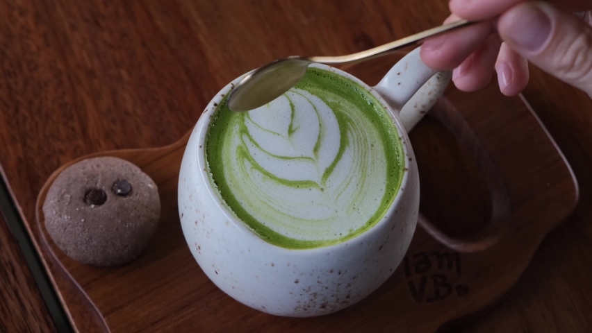 Human hand mixing foam on trendy vegan matcha latte with a spoon, detox hot drinks in a hipster cafe | Shutterstock HD Video #1085720537