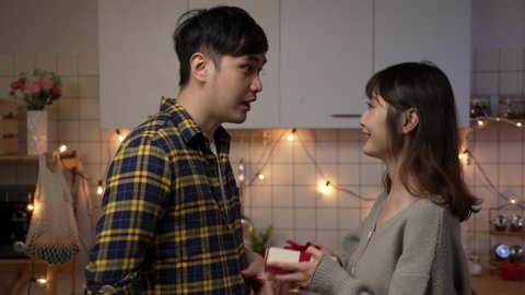 slow motion of asian boyfriend surprising his girlfriend with gift and rose flower at home. happy young couple kissing while celebrating valentine’s day at home