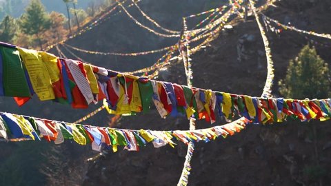 Slow motion shot of colorful Buddhist Tibetan prayer flag in front of mountains at Pangan Nyingmapa Monastery in Patlikuhal village near Manali, Himachal Pradesh, India