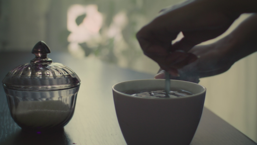 An African woman stirs sugar in a cup of hot tea in the morning before work.