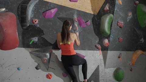 Female climber training on a climbing wall, young woman practicing rock-climbing, mountaineer training, moving up.