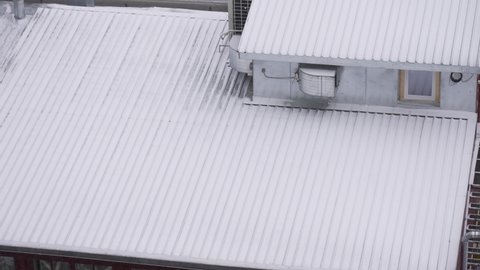 Top view slow motion 4k stock video footage of roof of small rural house covered with thin layer of fresh white snow. Snowflakes falling down on earth during winter snowfall