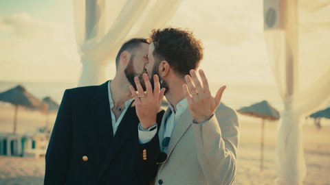 Portrait of a Happy Just Married Handsome Gay Couple in Love Showing Off Their Gold Wedding Rings. Two Attractive Queer Men in Suits Smile and Pose for Camera. LGBTQ Relationship and Family Goals.