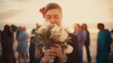 Portrait of a Beautiful Bride in Stylish Black Suit and Bow Tie Tossing Bridal Bouquet and Passing Good Fortune to Happy Multiethnic and Diverse Friends. LGBTQ Relationship, Family and Love Goals.