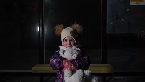 the child is alone at the bus stop and hugs the bear