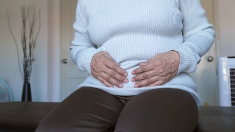 Elderly woman having painful stomach ache sitting on sofa,Female suffering from abdominal pain,Period cramps,Hands squeezing belly,Stomach pain,Menstruation