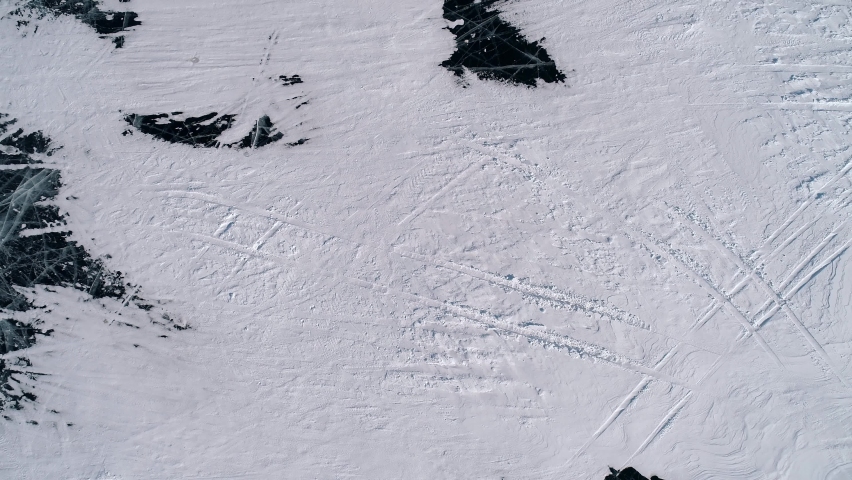 Aerial over the blue snowy cracked ice of Baikal. The rocky cliff in lake Baikal. Tourists walking around the cliff. Winter landscape of frozen Baikal. Popular tourist spot