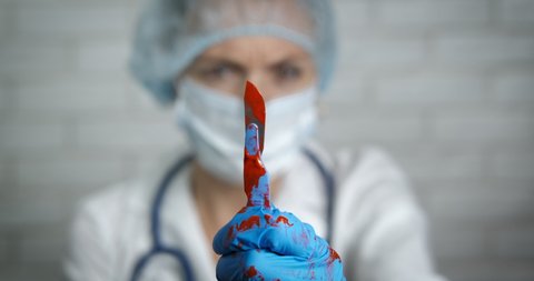 Scalpel after operation. A doctor woman in uniform hold a bloody scalpel after operation. A concept of medical work in the hospital.
