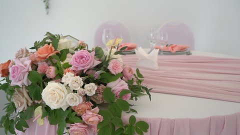 Served table in restaurant for dinner, lunch, celebration. White tablecloth, plates, napkins, glasses, chairs. Holiday. No people and food. Decorated with pink flowers for wedding in tent pavilion.