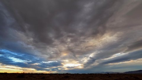 Dramatic overcast sunset sky above the Mojave Desert's harsh and rugged landscape - wide angle time lapse