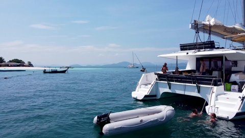 Phuket, Thailand, 20, January, 2022:
Sailing catamaran is anchored, rear view, the sailboat is standing in the sea, people are boarding after swimming
