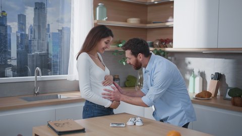 Caucasian family. Pregnant young caucasian wife expecting child laughing with her husband talking showing pregnancy tummy. Fun communication. Parents.