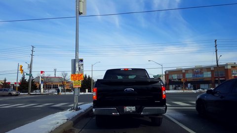 Toronto, Ontario, Canada - February 15th, 2020. Driver Point of View Waiting at Left Turn Lane at City Suburb Street Intersection. Drive Car Vehicle Wait Surrounded By Retail Stores and Traffic.