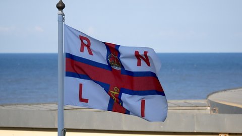Cromer, Norfolk, United Kingdom. Circa May 2021. Royal National Lifeboat Institution - RNLI - flag flying against blue sky and blue sea.